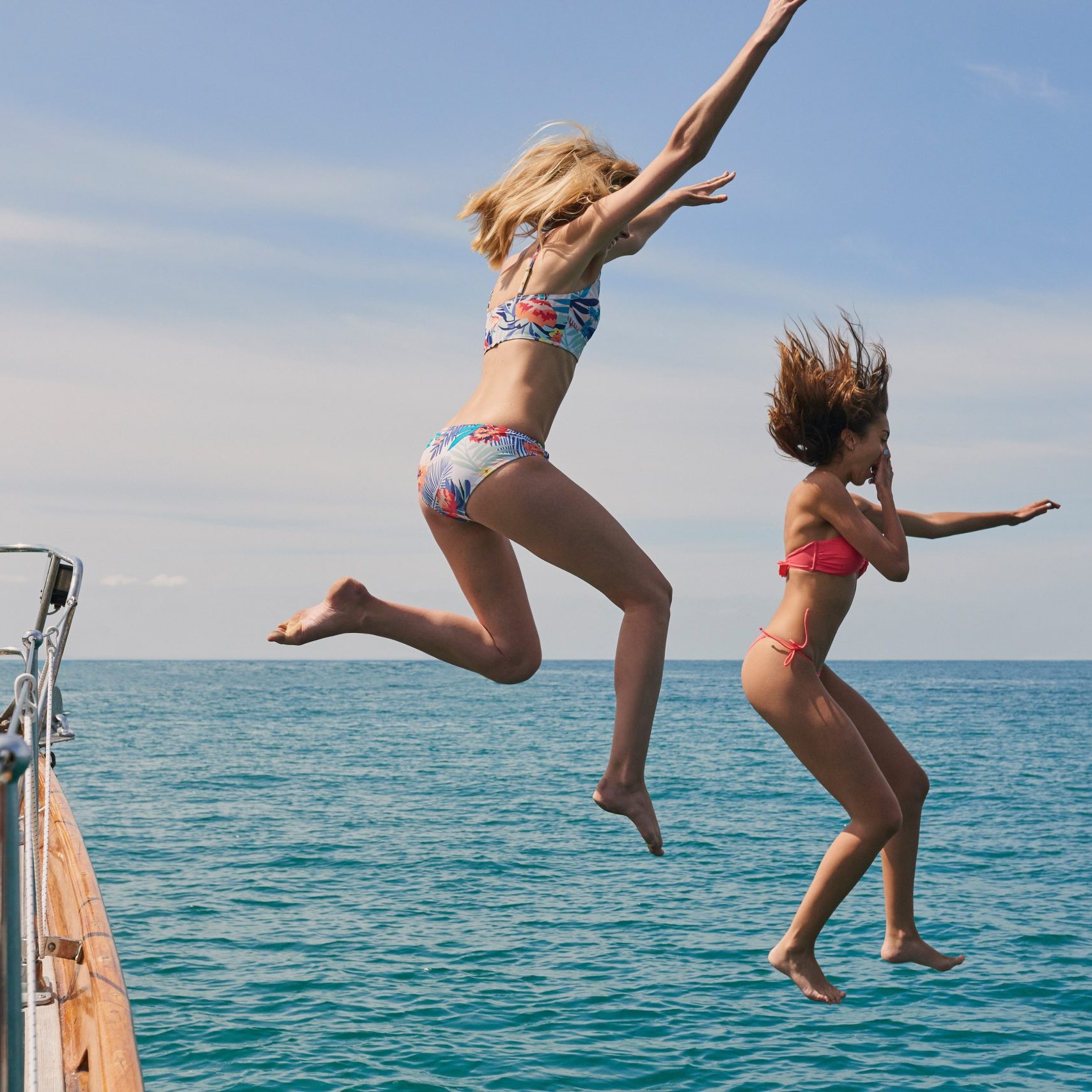 Excited women jumping from boat to swim in the ocean. Cheerful women jumping from boat during cruise to swim in the ocean